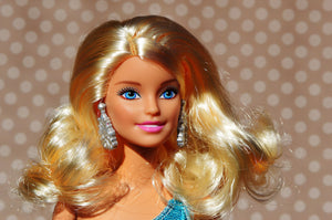 Image of Barbie Doll from shoulders up, with fake synthetic blonde hair. Illustrating how synthetic hair would look with clip in hair extensions. At LUSHIERE we only sell clip in hair extensions made of real human hair.