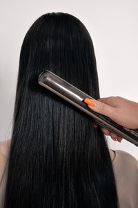 Image of someone using hair straighteners on long black hair showing how LUSHIERE clip in hair extensions can be heat styled